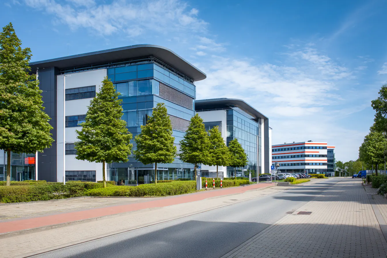 Moderne Bürogebäude mit Glasfassaden und Bäumen, Straße mit Kopfsteinpflaster und Gehweg.